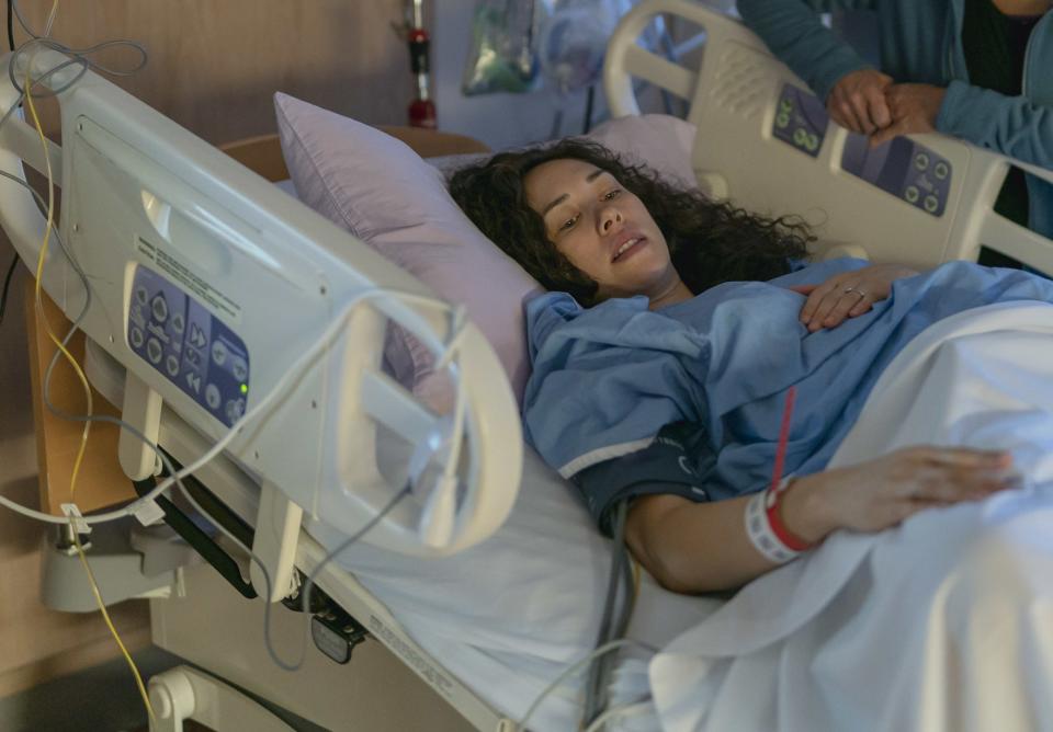 A soon to be mother is in a hospital bed waiting to give birth with her own mother standing at her bedside in support