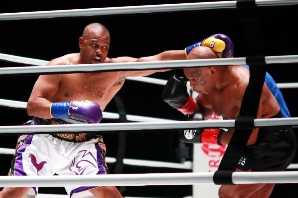 One boxer holds out his left arm as another boxer bends down.