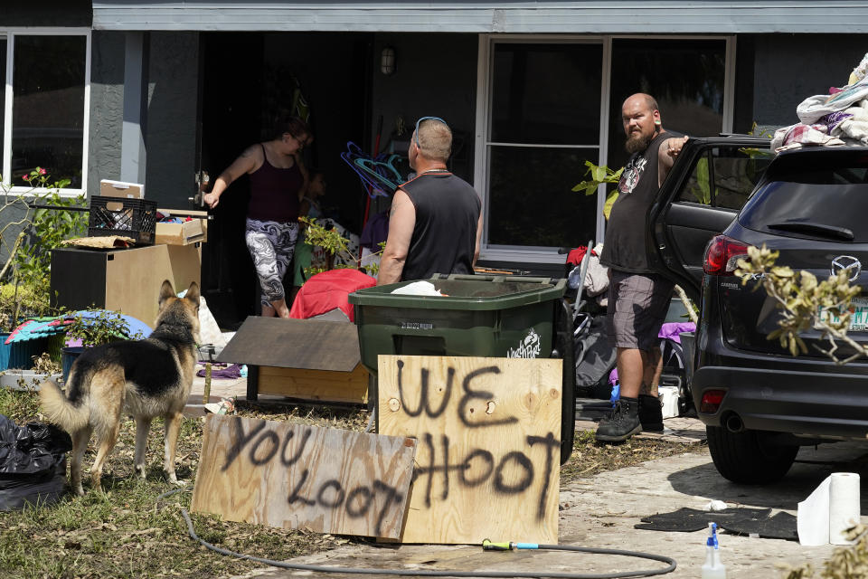 Residents behind a "you loot, we shoot" sign clean up their flooded property Tuesday, Oct. 4, 2022, in North Port, Fla. Residents in the area continue cleaning up after Hurricane Ian came ashore along Florida's west coast last week. (AP Photo/Chris O'Meara)