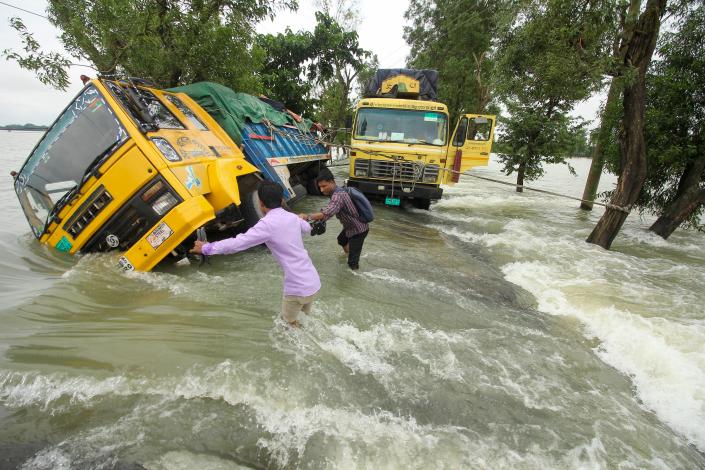 People wade past stranded trucks on a flooded street in Sunamganj, Bangladesh, on June 21