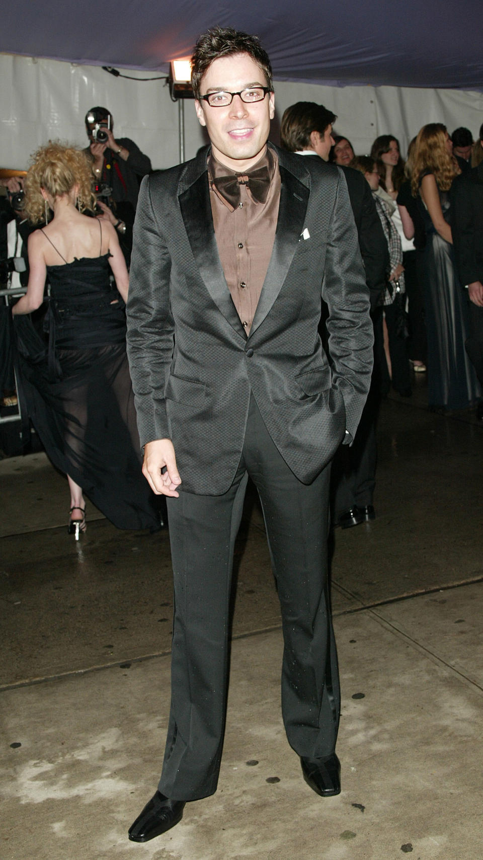 Man in black suit with satin lapels and a brown shirt posing on a carpet