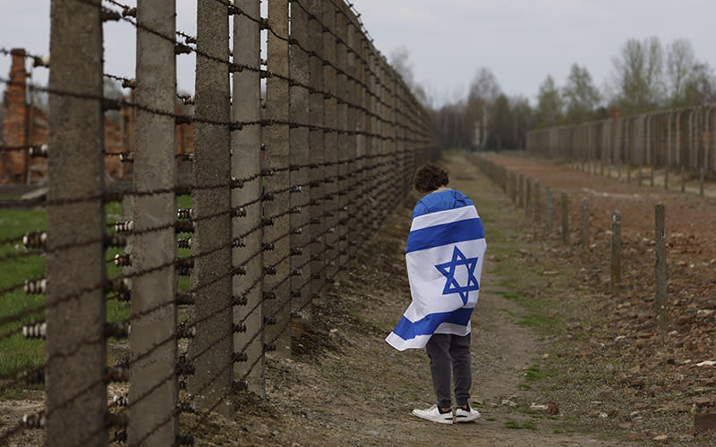 A man with an Israeli flag stands outside of the fence of a former Nazi-run death camp