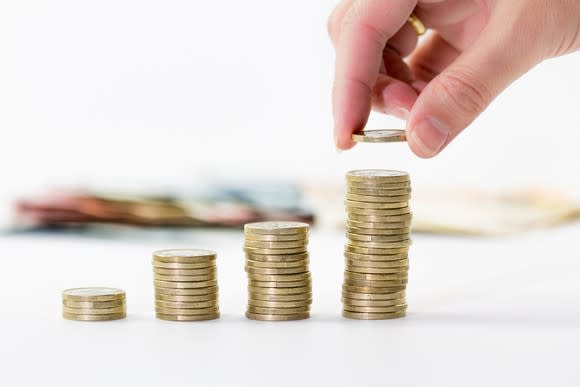 Successively larger stacks of gold coins with a hand placing another coin on the largest stack