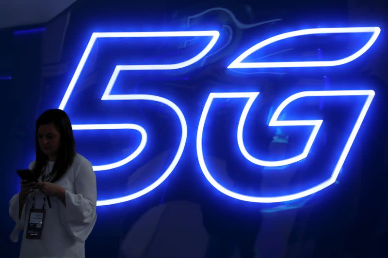 FILE PHOTO: A woman looks at her mobile phone next to a 5G sign at the Mobile World Congress in Barcelona