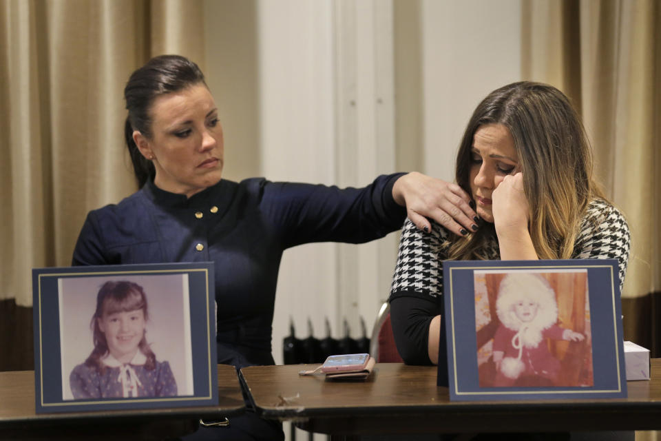 Teresa Forteny-Miller, left, comforts her sister Carolyn Fortney as they sit behind pictures of themselves as children as they listen to their other sisters speak during a news conference in Newark, N.J., Monday, Dec. 2, 2019. Two of the sisters from Pennsylvania are suing the Archdiocese of Newark and the Diocese of Harrisburg, Pennsylvania. They allege clergy in Newark knew a priest had sexually abused children before he moved to Harrisburg and abused them and their sisters for years. Lawsuits alleging sexual abuse by Roman Catholic clergy are taking center stage in New Jersey as the state's relaxation of statute of limitations rules takes effect. (AP Photo/Seth Wenig)