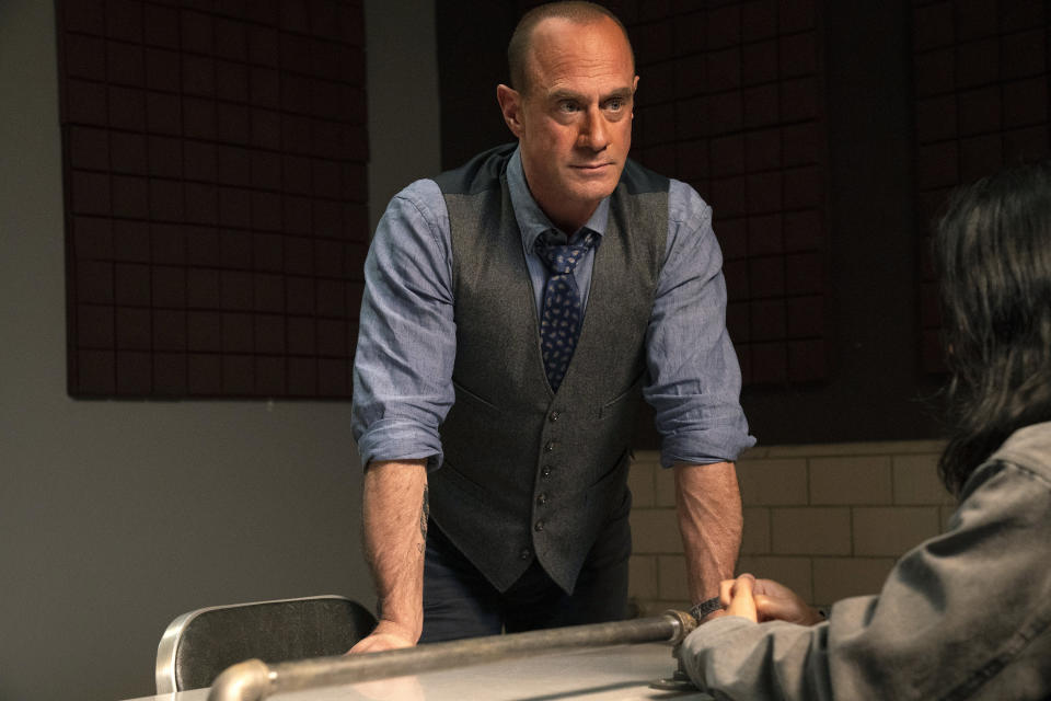 Meloni in suit sans coat with sleeves rolled up, leaning on a table in an interrogation room in front of a suspect