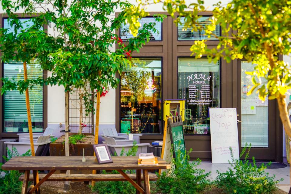 Culdesac Tempe: Ein Laden mit braunen Türen hinter einem Tisch im Freien, Bäumen und Sträuchern