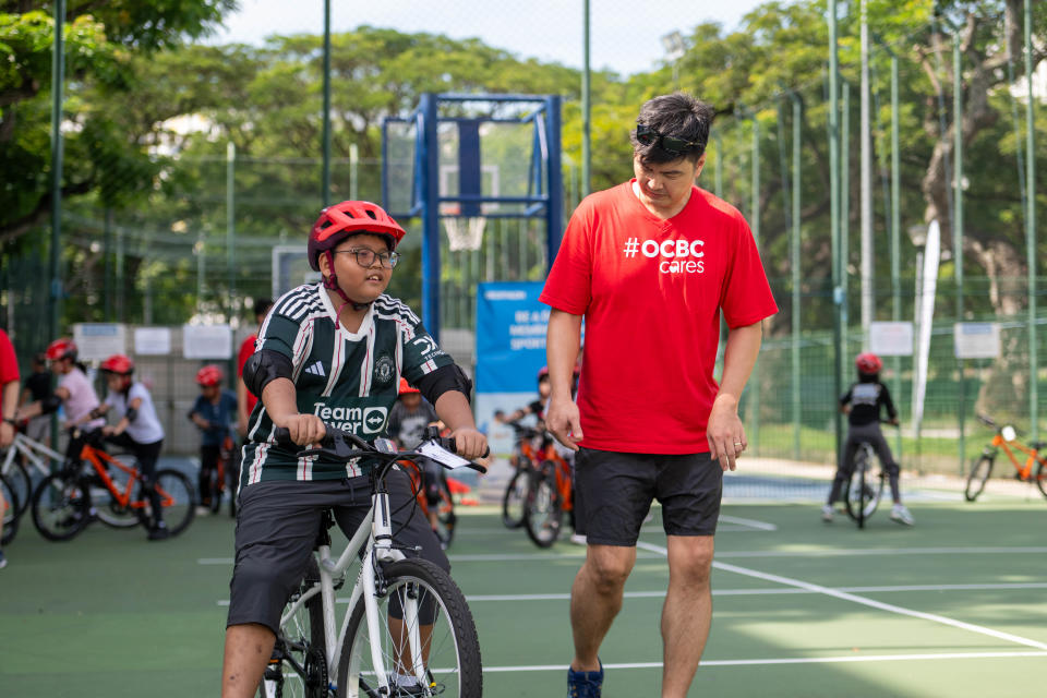 Muhammad Arsyad Zafri Abdullah (left) learning how to ride a bicycle with help from a volunteer from OCBC at Teach-a-Child-to-Cycle 2024. (PHOTO: OCBC Cycle 2024)