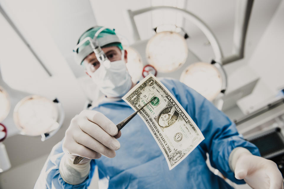 Surgeon pulling a dollar bill out of a patient with forceps.