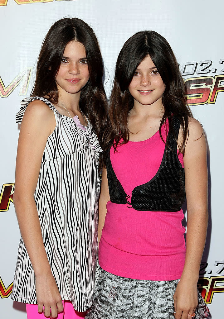 Two young female celebrities at an event; one in a striped top with ruffles, the other in a pink tank top and black vest