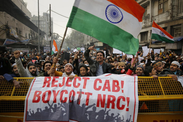 FILE - Indians wave national flags and shout slogans behind a police barricade during a protest against the Citizenship Amendment Act in New Delhi, India, Friday, Dec. 20, 2019. The new law provides a fast track to naturalization for some migrants who entered the country illegally while fleeing religious persecution. But it excludes Muslims, which critics say is discriminatory and a violation of India's Constitution. (AP Photo/Altaf Qadri, File)
