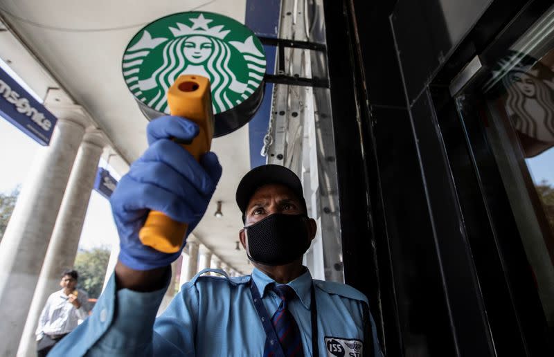 A private security guard checks the body temperature of a customer outside a Starbucks coffee shop, as a precaution against the spread of coronavirus, in New Delhi