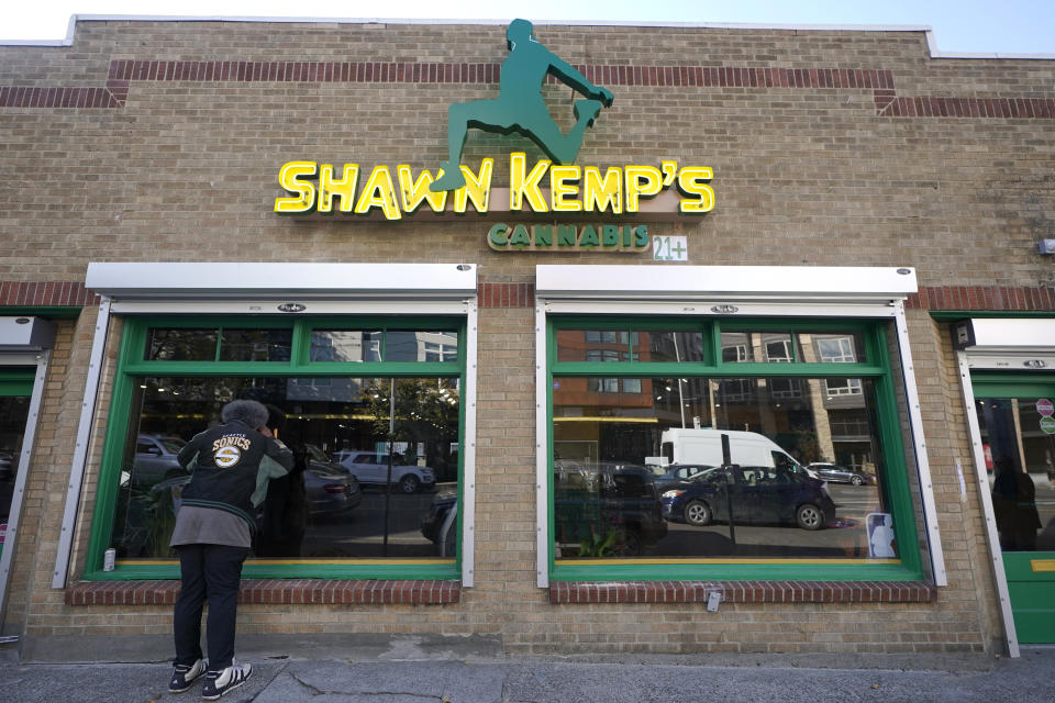 Kris "Sonics Guy" Brannon, a Seattle SuperSonics superfan, looks in the window of Shawn Kemp's Cannabis, the marijuana dispensary owned by Shawn Kemp, a former NBA basketball player for the SuperSonics and several other teams, along with with several business partners, before the store's grand opening, Friday, Oct. 30, 2020, in downtown Seattle. (AP Photo/Ted S. Warren)