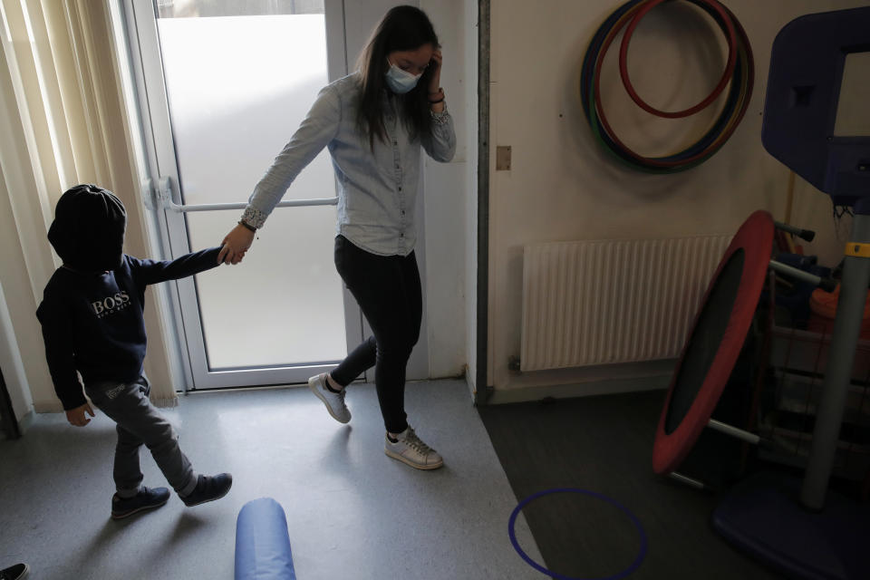 Maelle Allanore, a psychomotor therapist holds the hand of a boy as they walk in the pediatric unit of the Robert Debre hospital, in Paris, France, Tuesday, March 2, 2021. (AP Photo/Christophe Ena)
