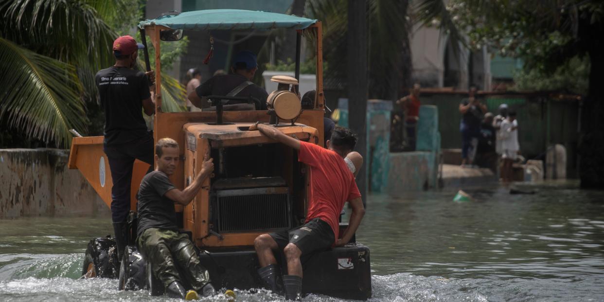 Workers hang onto a dump truck in a flooded street.