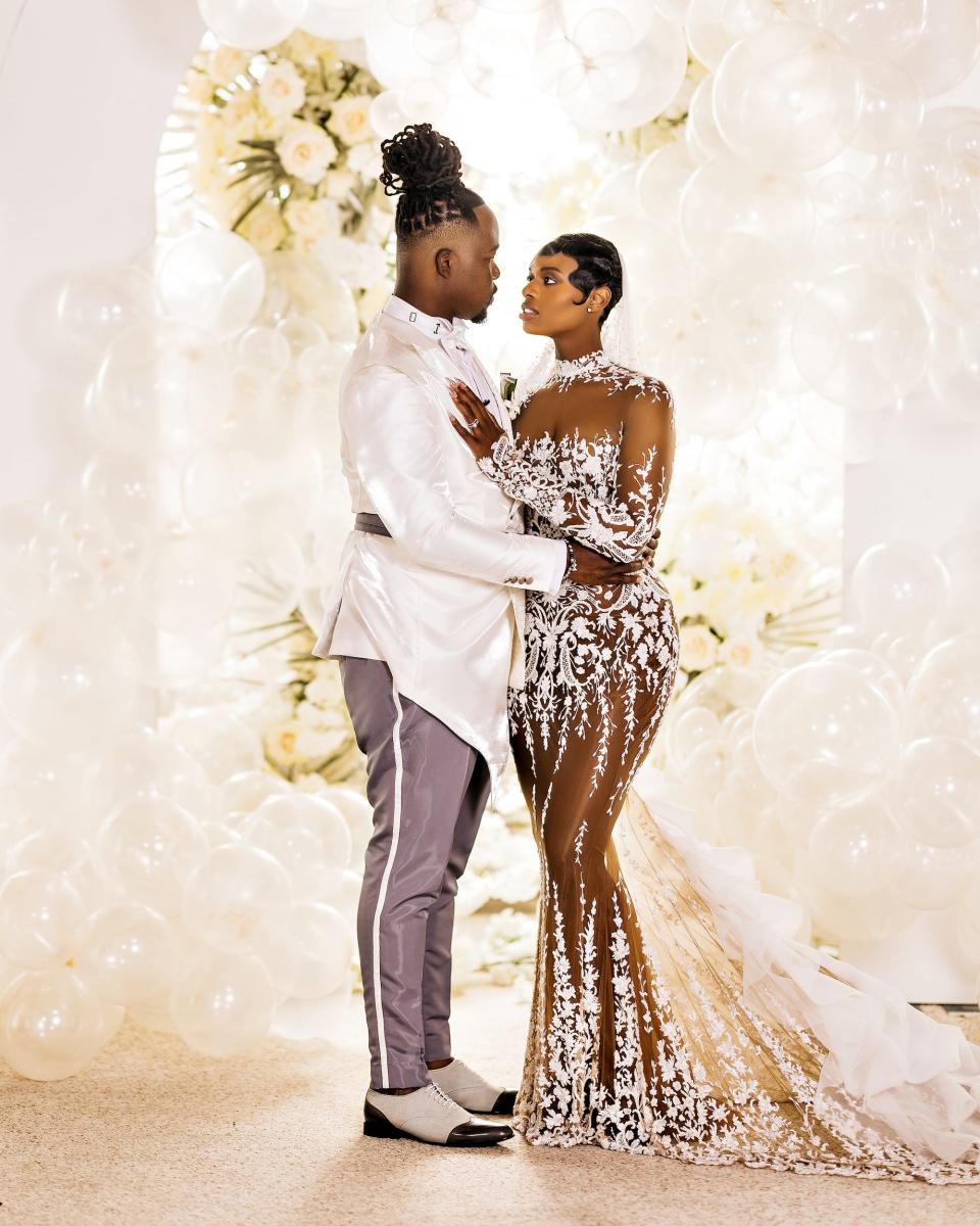 A bride and groom look at each other in front of a balloon arch.