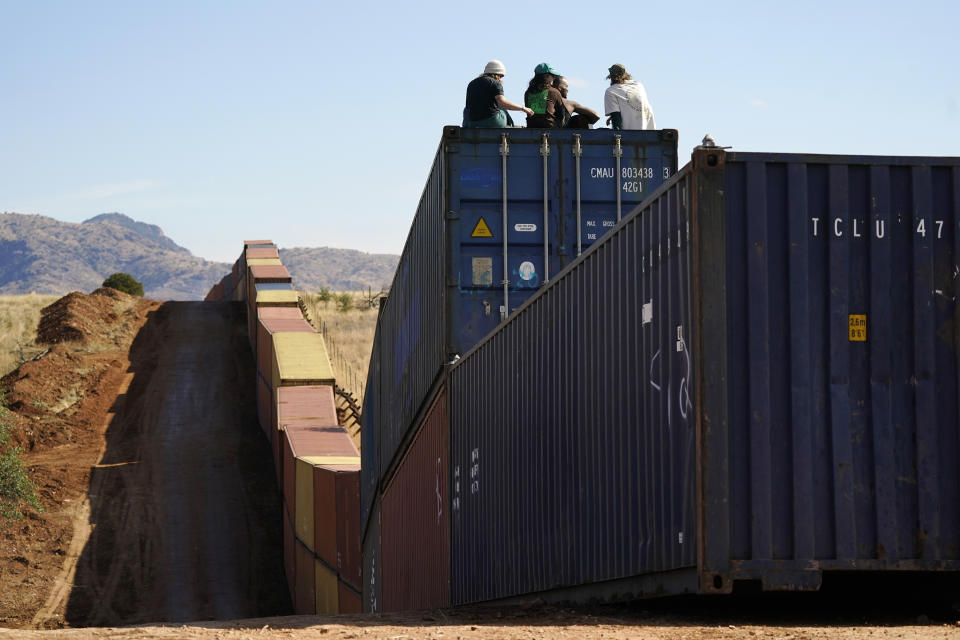 Activists sit on newly installed shipping containers along the border creating a wall between the United States and Mexico in San Rafael Valley, Ariz., Thursday, Dec. 8, 2022. Work crews are steadily erecting hundreds of double-stacked shipping containers along the rugged east end of Arizona’s boundary with Mexico as Republican Gov. Doug Ducey makes a bold show of border enforcement even as he prepares to step aside next month for Democratic Governor-elect Katie Hobbs. (AP Photo/Ross D. Franklin)