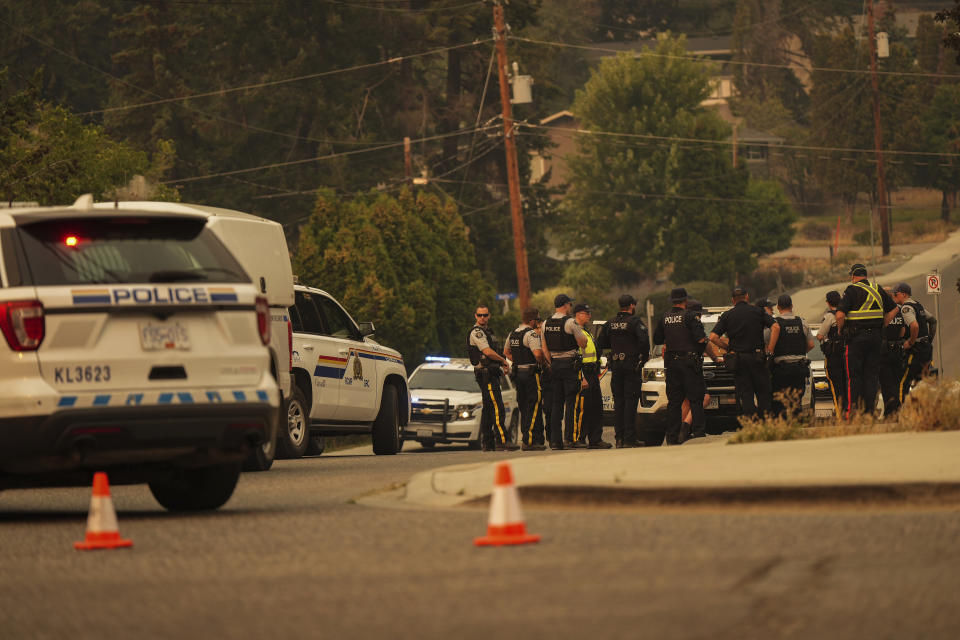 RCMP officers meet at a roadblock after evacuating the Wilden neighbourhood near Knox Mountain due to a wildfire burning above homes in Kelowna, British Columbia, Friday, Aug. 18, 2023. (Darryl Dyck/The Canadian Press via AP)