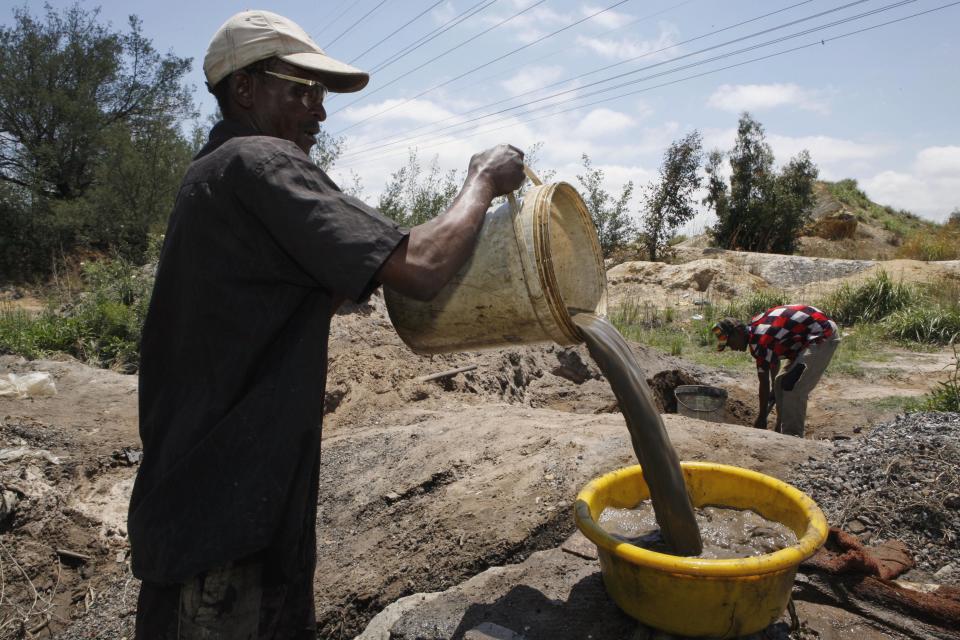 In this Friday Nov. 2, 2012 photo Daniel Mazibuko, pours heavy buckets of water heavy with soil into a yellow plastic bowl during their illegal gold mining in Roodepoort, South Africa. South Africa’s abandoned gold mines provide many of the country’s unemployed and immigrants with ways to earn money when odd jobs don’t provide a sustainable living. With an increased unemployment rate of 25.5 percent, many turn to illegal gold mining off a main road outside Johannesburg which hosts dozens of men hoping to strike it rich. (AP Photo/Themba Hadebe)