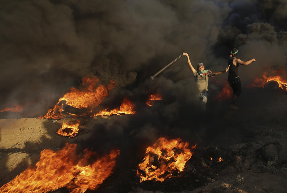 FILE-- In this Sept. 7, 2018 file photo, a protester hurls stones while others burn tires near the fence of Gaza Strip border with Israel, during a protest. Palestinians in the Gaza Strip have coped with shortages of just about everything in more than a decade of border closures -- from chocolate to medicines to fuel and building supplies. Now, the past six months of protests against an Israeli-Egyptian blockade have added an unexpected item to the list of those in short supply: car tires. (AP Photo/Adel Hana, File)