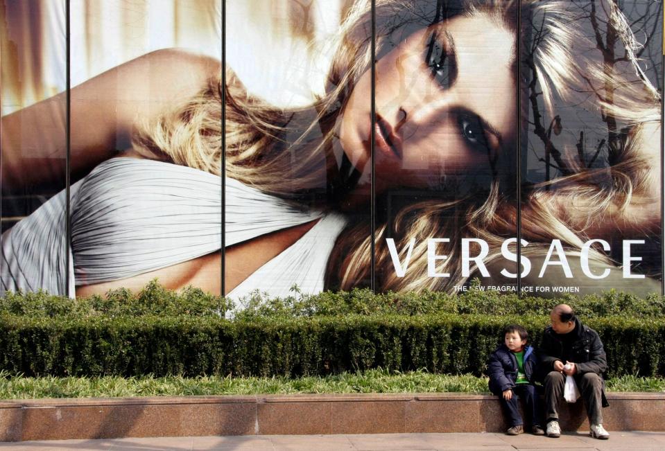 In this 2008 file photo, a child and a man sit in front of an advertisement for the Italian fashion house Versace in Shanghai, China. The company has apologized in China for selling T-shirts that attached country names to cities.