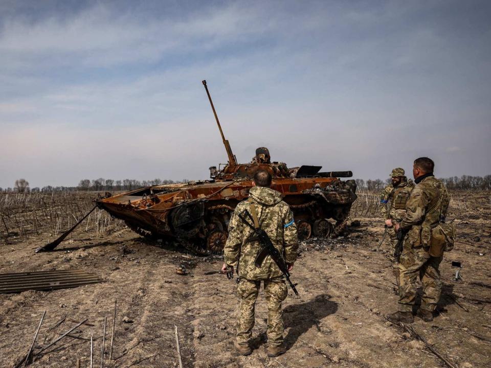 Ukrainian soldiers standing near a burnt Russian tank