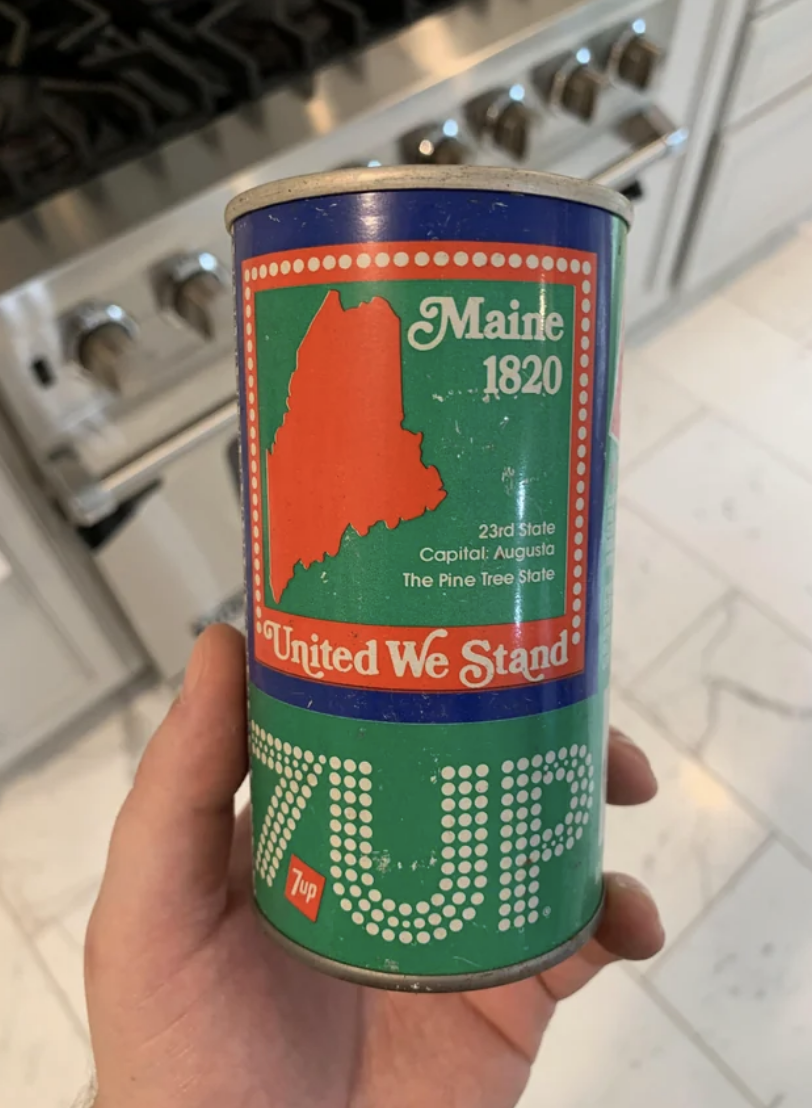 Vintage Maine-themed soda can with state outline, slogan "United We Stand," held in a kitchen