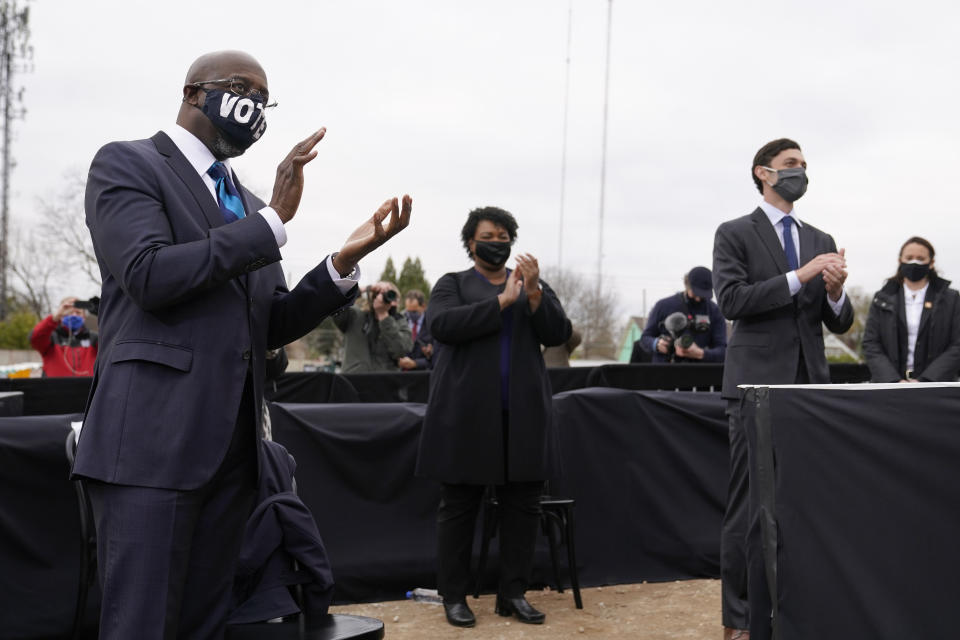 Georgia Democratic candidate for U.S. Senate Raphael Warnock, left, applauds as President-elect Joe Biden speaks at a drive-in rally for Warnock and Jon Ossoff, Tuesday, Dec. 15, 2020, in Atlanta. Standing with Warnock are Stacey Abrams, center, and Georgia Democratic candidates for U.S. Senate Jon Ossoff. (AP Photo/Patrick Semansky)