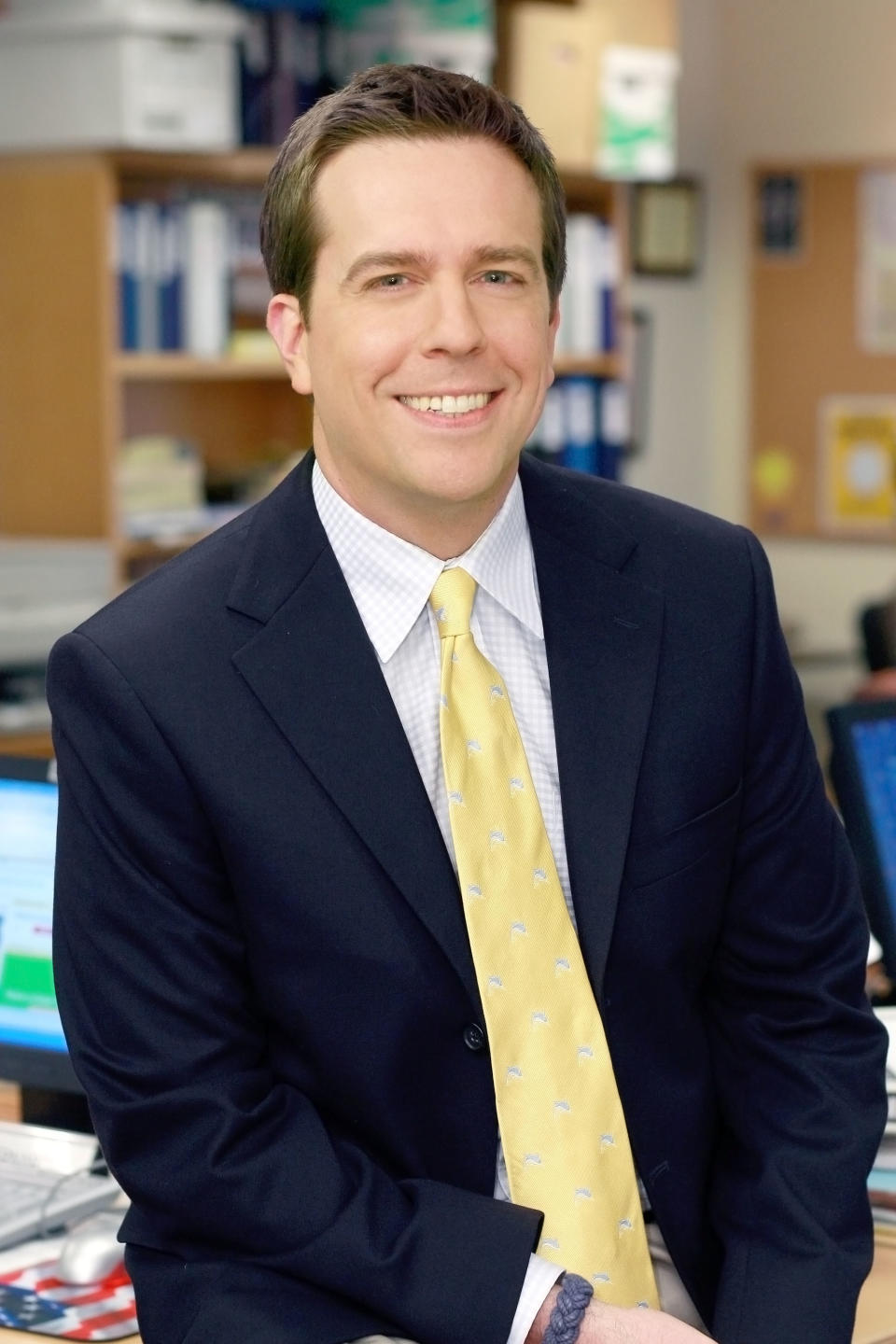 andy sitting on top of his desk in a suit