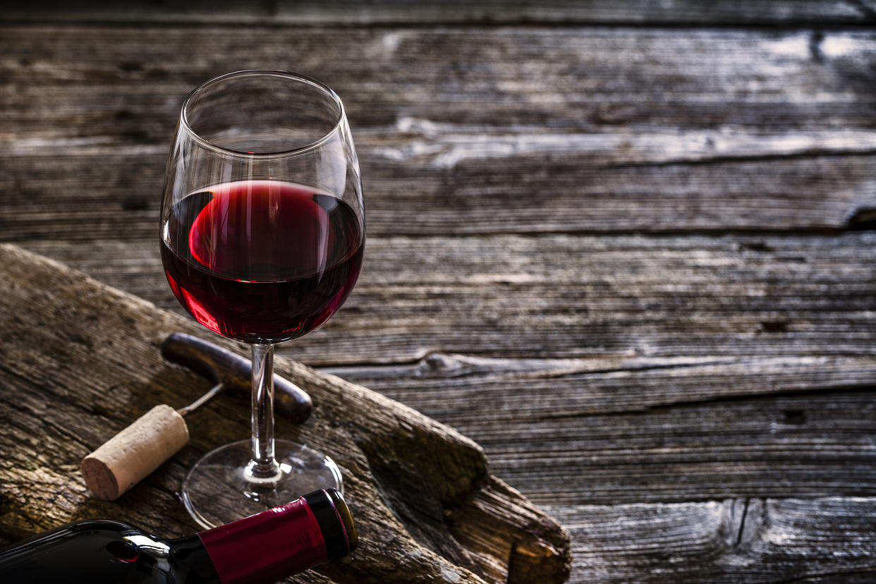 Wine bottle, wineglass with a corkscrew and a cork stopper shot on rustic textured wooden table. The composition is at the left of the table the table. Copy space available for text and/or logo. Predominant color is brown. Low key DSRL studio photo taken with Canon EOS 5D Mk II and Canon EF 100mm f/2.8L Macro IS USM.