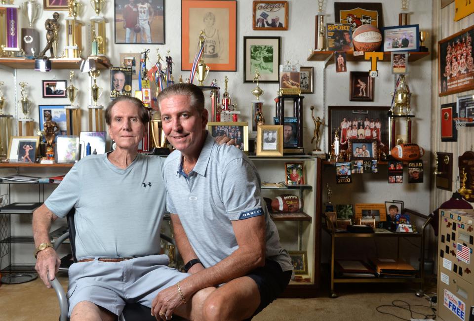 Long-time Sarasota basketball coach Kerry Baker, poses for a photo with his son, Steve, surrounded by years and years of sports memorabilia displayed in a room in his home.