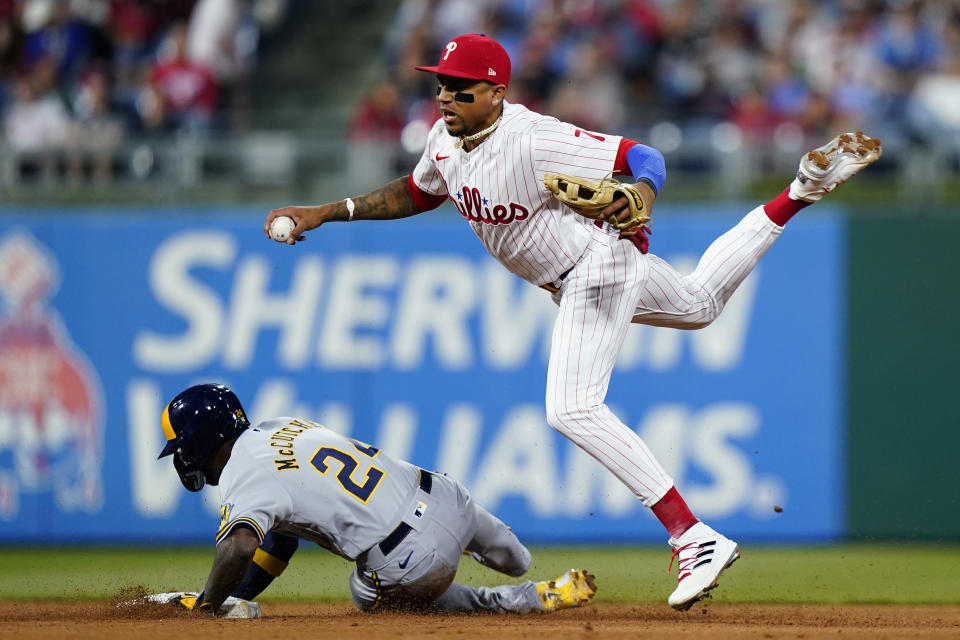 Philadelphia Phillies shortstop Johan Camargo, right, falls after forcing out Milwaukee Brewers' Andrew McCutchen at second base on a double play hit into by Milwaukee Brewers' Willy Adames during the fifth inning of a baseball game, Friday, April 22, 2022, in Philadelphia. (AP Photo/Matt Slocum)