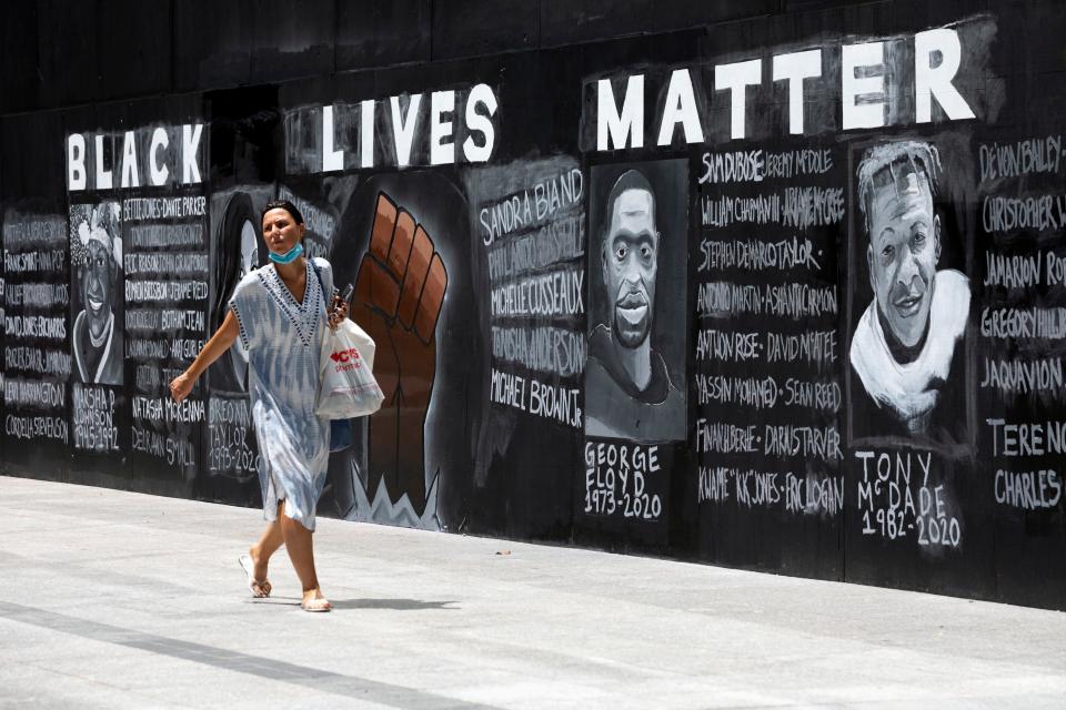 A woman walks past a "Black Lives Matter" mural painted on the boarded-up Apple Store, June 6, 2020, in Boston.