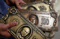 <p>Russian hacker Sergey Pavlovich, better known by his former online alias Police Dog, holds a mock money printing plate with Russian President Vladimir Putin, bottom, and US President Donald Trump, center, faces in place of Benjamin Franklin during an interview with the Associated Press in Moscow, Russia, Aug. 9, 2017. (Photo: Pavel Golovkin/AP) </p>