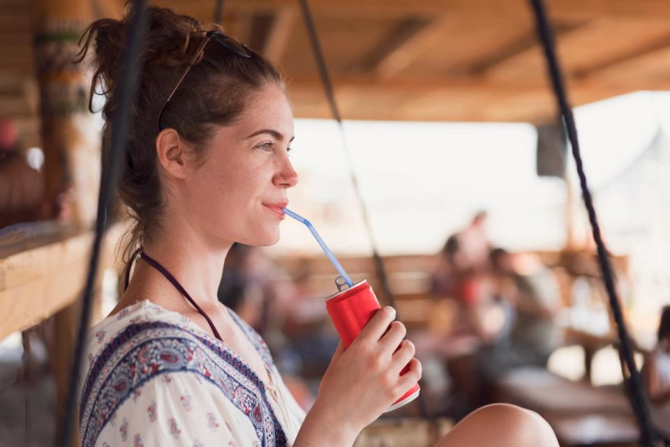 A person sitting down drinking a can of soda through a straw.