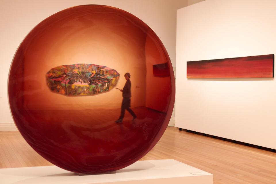 A woman walks between the sculpture 'Red Concave Circel' from 1970 by artist De Wain Valantine and the paintings 'Black Tear' from 1969 by Ronald Davis at the left side and '90% Devil 10% Angel' from 1982 by Ed Ruscha, at right side, during a press preview of the exhibition 'Pazific Standart Time' in Berlin Wednesday, March 14, 2012. The exhibition that offers viewers a primer on three decades of Los Angeles' diverse art scene and stems from a decade of research is going on show in Berlin from March 15. until June 10, 2012. .(AP Photo/Markus Schreiber)