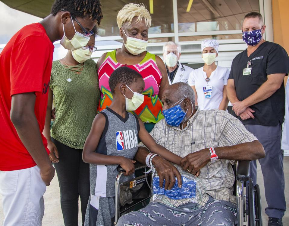 James Gardner, 77, goes home after battling COVID-19 for a month at Jackson South Medical Center, Thursday, Aug. 27, 2020 in Miami. Greeting him outside the hospital is his adopted son Shaquille Gross, 7, and the rest of his family, left to right, Noel Gross, 16, Kendra Gross, 17, his wife Maggie Gross Gardner, 75, as the medical staff at the hospital sends his home.(Al Diaz/Miami Herald via AP)
