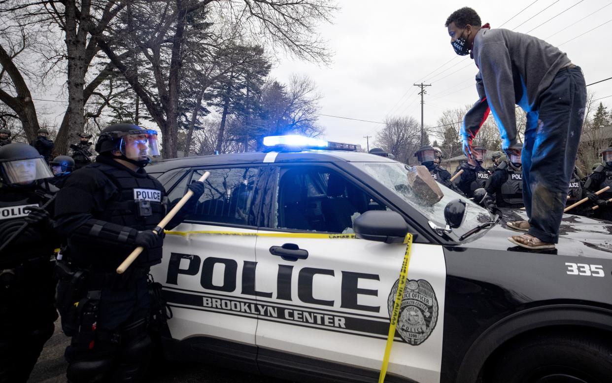 A man stands atop a police car after throwing a brick at the windshield near the site of a shooting involving a police officer, Sunday, April 11, 2021, in Brooklyn Center, Minn.