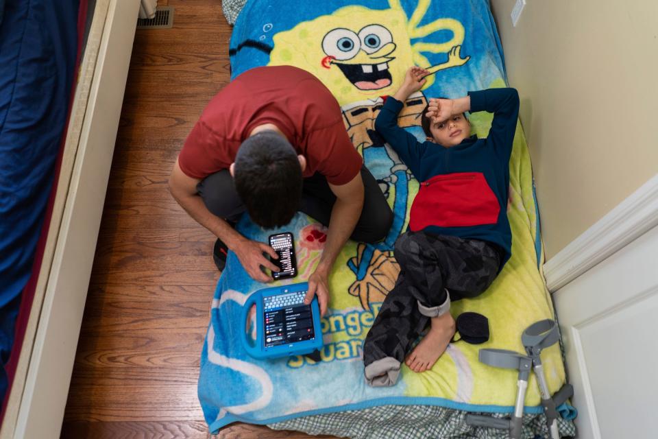 Saleh Humaid, 8, of Gaza, lays down on an inflatable mattress while Mohamed Hamed, 21, of Dearborn Heights, works to change the language on an iPad for Humaid to use after arriving the previous night to be hosted at Hamed's home on Tuesday, June 13, 2023. Humaid traveled to the U.S. with the help of the PCRF to receive free medical treatment and a new prosthetic leg along with rehab before returning home after losing part of his leg from shrapnel when a drone strike hit a car as he passed it while driving with his father in Gaza.