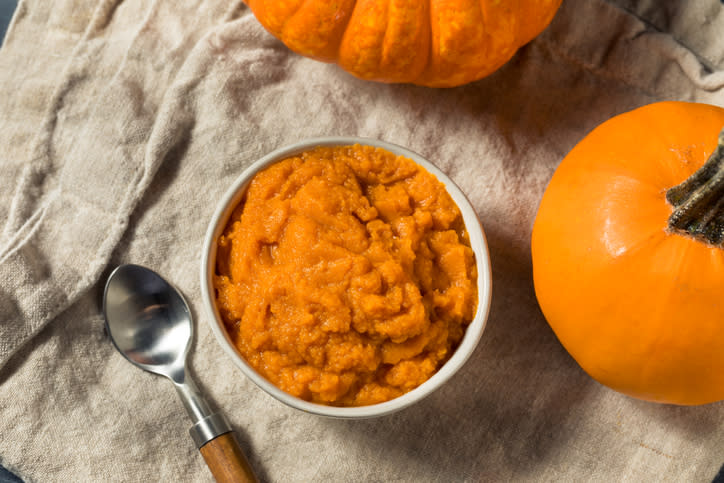 Pumpkin puree i n a bowl surrounded by pumpkins