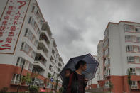 An ethnic minority woman carries her child past apartment houses with China's propaganda slogan in Yuexi county, southwest China's Sichuan province on Sept. 11, 2020. China's ruling Communist Party says its initiatives have helped to lift millions of people out of poverty. Yi ethnic minority members were moved out of their mountain villages in China’s southwest and into the newly built town in an anti-poverty initiative. The slogan, left, reads: "Preschool speaks Mandarin, not afraid of talking and reading." (AP Photo/Andy Wong)