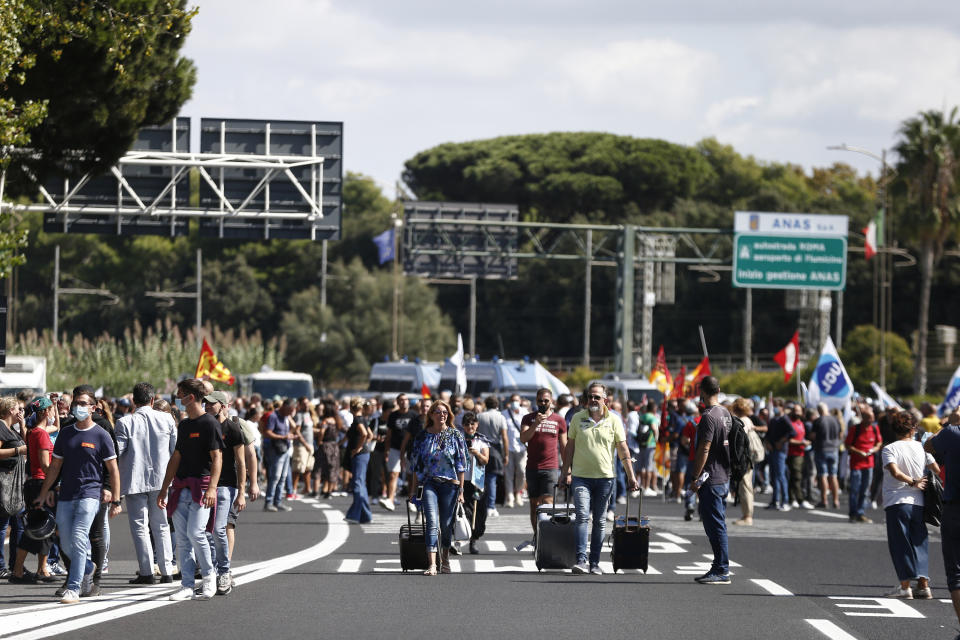 Passengers push their trolleys as Alitalia workers blocked the road leading to the Rome Leonardo Da Vinci international airport following a protest in Fiumicino, Friday, Sept. 24, 2021. Alitalia, which has been in the red for more than a decade, is due to formally exit the airline market next month and be replaced by a new national carrier ITA, or Italy Air Transport. The European Commission has given the go-ahead to a 1.35 billion euro ($1.58 billion) injection of government funding into the new airline, but ITA is only planning to hire around a quarter of the estimated 10,000 Alitalia employees. (Cecilia Fabiano/LaPresse via AP)