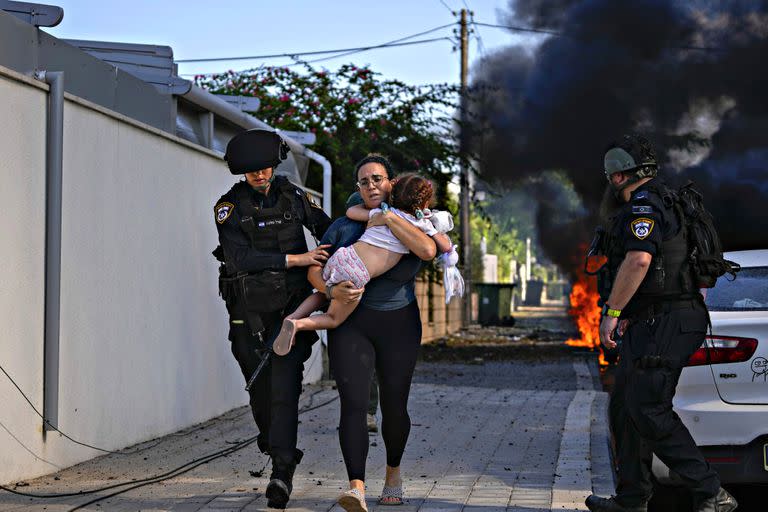 Agentes de policía israelíes evacuan a una mujer y un niño de un lugar alcanzado por un cohete lanzado desde la Franja de Gaza, en Ashkelon, sur de Israel, el sábado 7 de octubre de 2023.