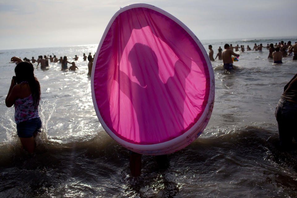 In this March 3, 2013 photo, a man is silhouetted in a wading pool as he cleans it out in the ocean waters off Agua Dulce beach in Lima, Peru. While Lima's elite spends its summer weekends in gate beach enclaves south of the Peruvian capital, the working class jams by the thousands on a single municipal beach of grayish-brown sands and gentle waves. On some weekends during the Southern Hemisphere summer, which runs from December until March, as many as 40,000 people a day visit the half-mile-long (kilometer-long) strip of Agua Dulce. Beachgoers arrive in groups of 20-30, hauling enormous pots of fragrant chicken and rice. (AP Photo/Rodrigo Abd)