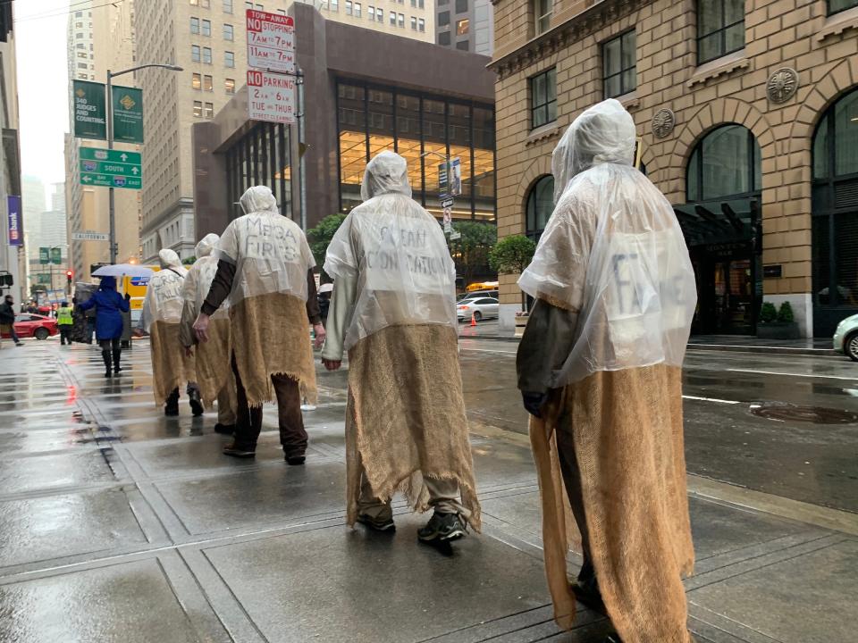 five people in burlap sacks medieval costume walking down rainy street