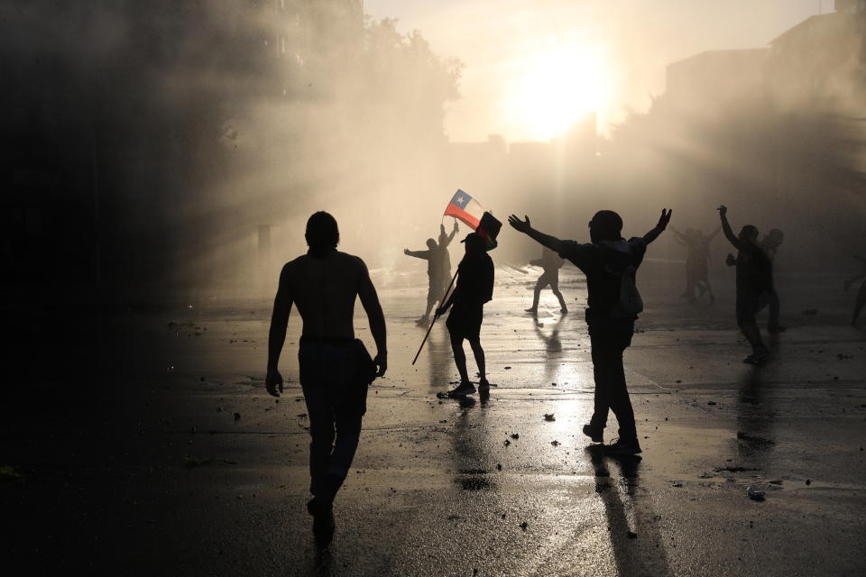 FILE - In this Oct. 31, 2019, file photo, demonstrators are sprayed by a police water cannon during an anti-government protest in Santiago, Chile. From Honduras to Chile, popular frustration with anemic economic growth, entrenched corruption and gaping inequality is driving the region’s middle classes to rebel against incumbents of all ideological bents in what has been dubbed by some the Latin American Spring. (AP Photo/Rodrigo Abd, File)