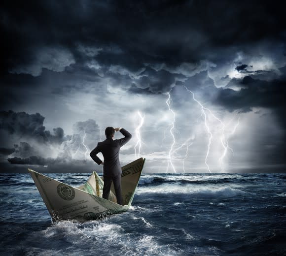 Man in suit standing on a paper boat made out of a dollar bill in a stormy sea