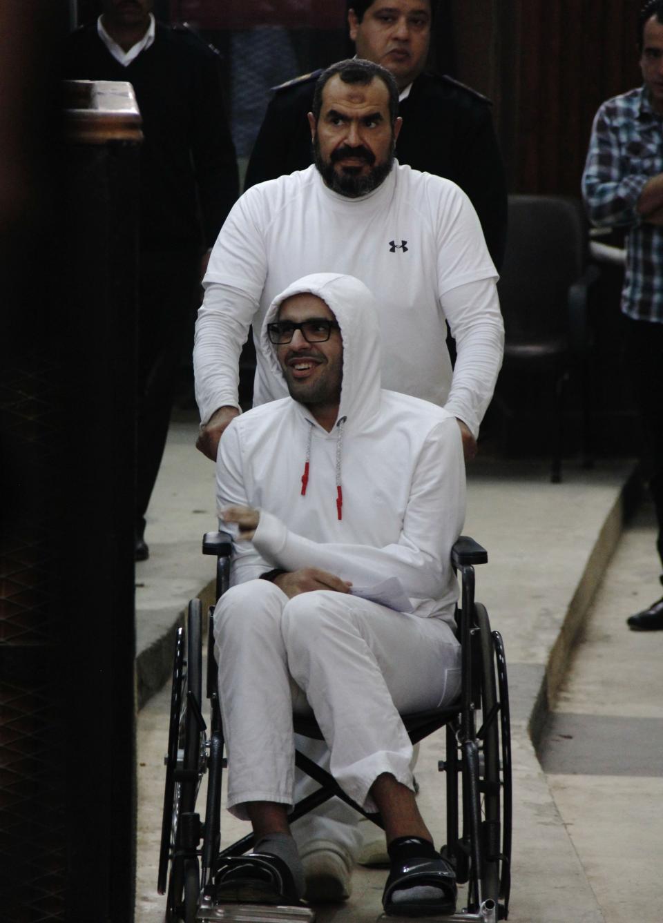 FILE - In this March 9, 2015 file photo, Mohamed Soltan, a dual U.S.-Egyptian citizen, is pushed by his father Salah during a court appearance in Cairo, Egypt. Human Rights Watch, an international rights group, said in a statement released Thursday, June 11, 2020, that Egyptian police raided the homes of two uncles of Soltan. On June 1, 32-year-old Soltan, now living in Virginia, filed a lawsuit against el-Beblawi accusing him of targeting him for attempted extrajudicial execution and torture while he was in detention in Cairo between 2013 and 2015. Under pressure from the Obama administration, Egypt released Soltan in 2015, although his father remains in prison. El-Beblawi currently lives in Washington, where he works as an executive director of the International Monetary Fund. (AP Photo/Heba Elkholy, File)