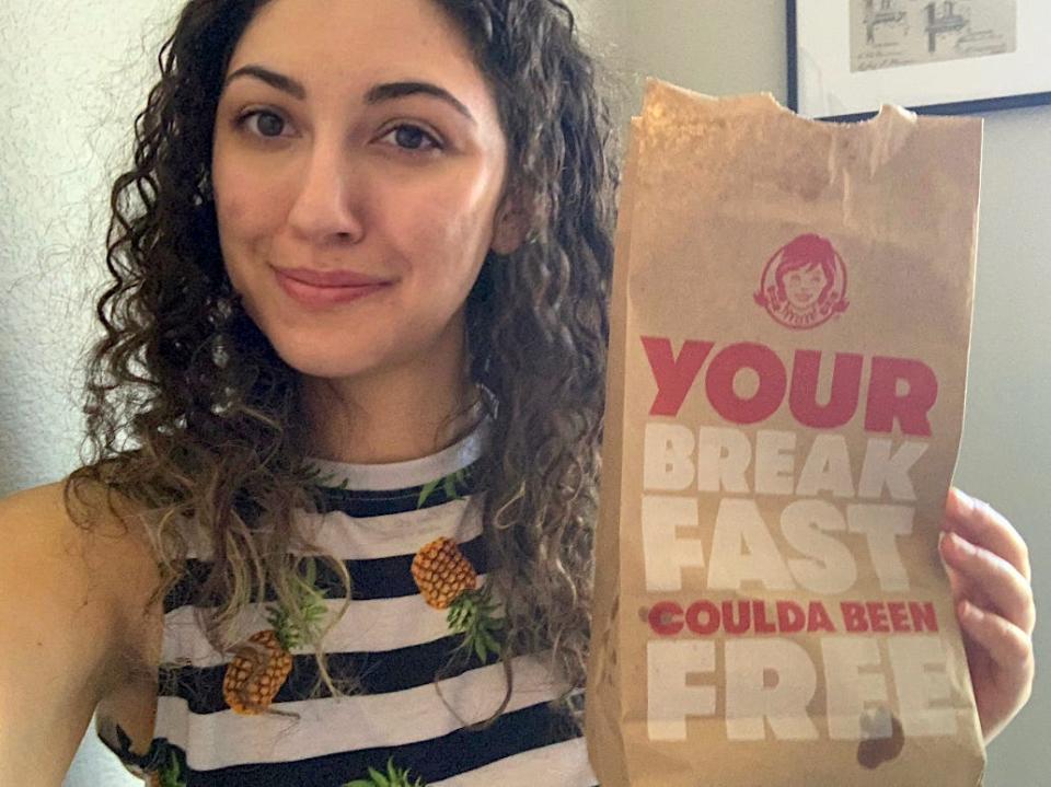 The writer holding a bag of Wendy's breakfast