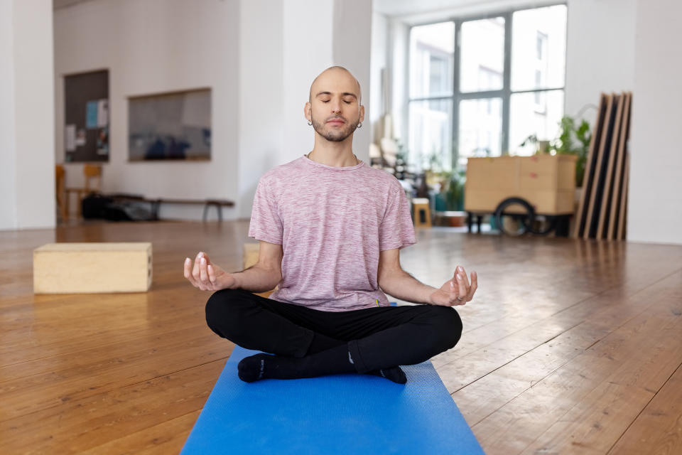 Hispanic man sitting in lotus pose in yoga class. Bald man wearing nose and ear piercing meditating in fitness studio.